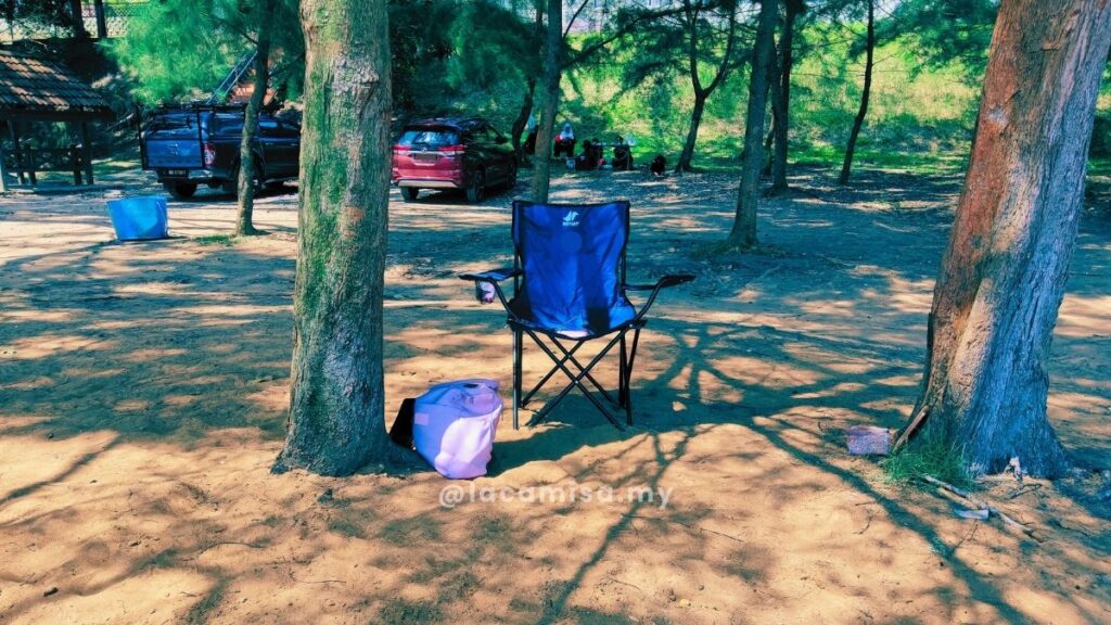 Portable folding camping chair set up under leafy trees.