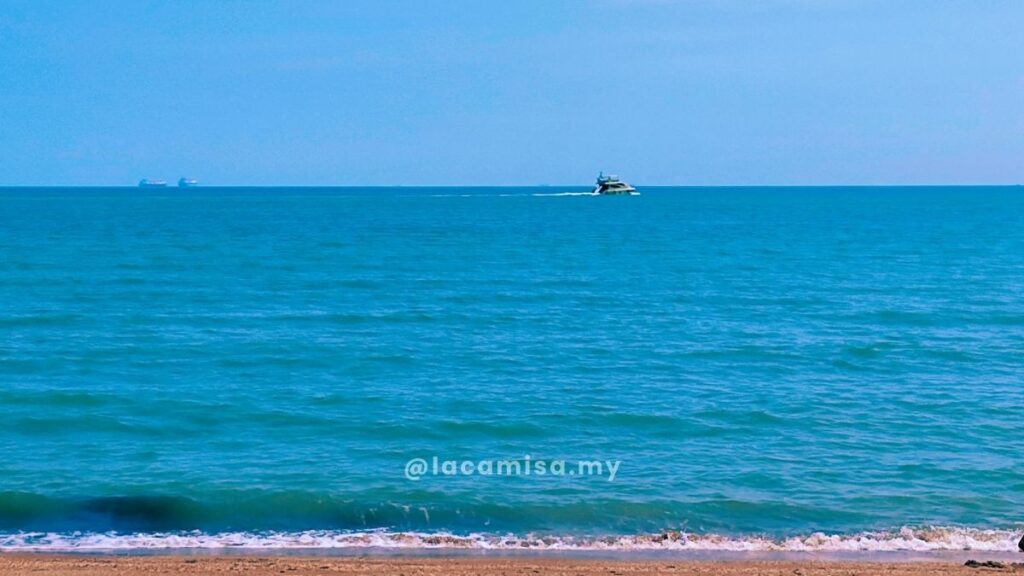 A large white cruiser boat sailing across the bright blue waters of the Malacca Strait seen from Monkey Bay Beach.